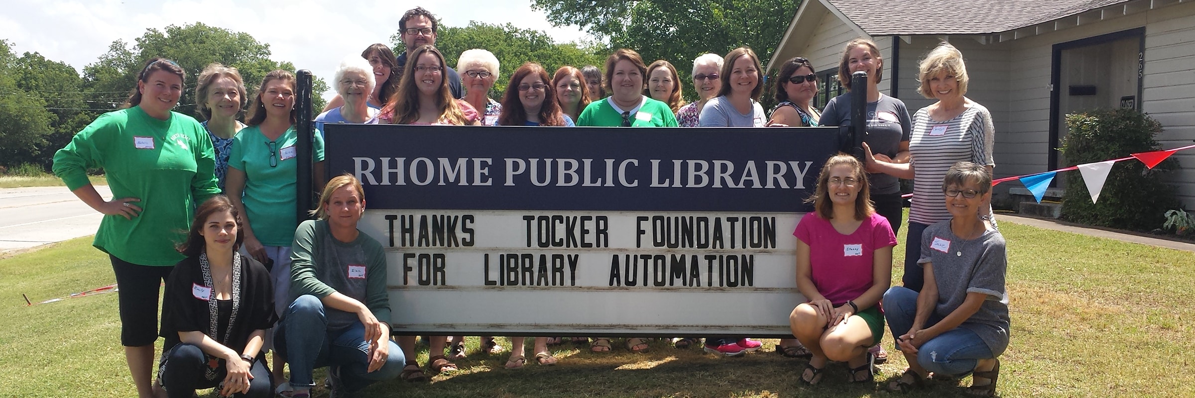 crowd posing next to Rhome Public Library signage: Thanks Tocker Foundation for Library Automation