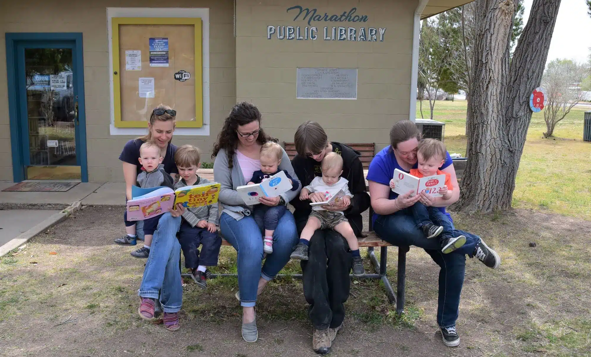 Four young mothers read to their babies on a bench outside the Marathon Public Library.