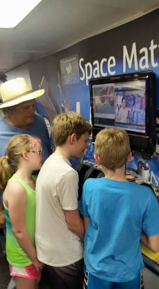 Three young kids and an adult looking at television screen at a space exhibit.